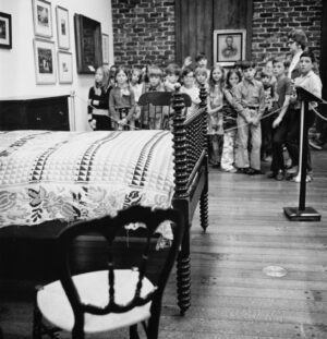 Lincoln's death bed on display with other furnishings to give the effect of the boarding house room. Schoolchildren stand behind a rope blocking off the exhibition. 