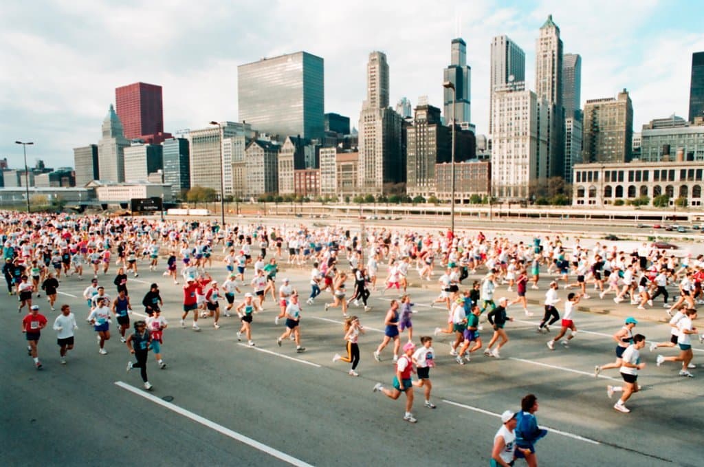 Color photograph of approximately one hundred runners on a city street with the Chicago skyline in the background.