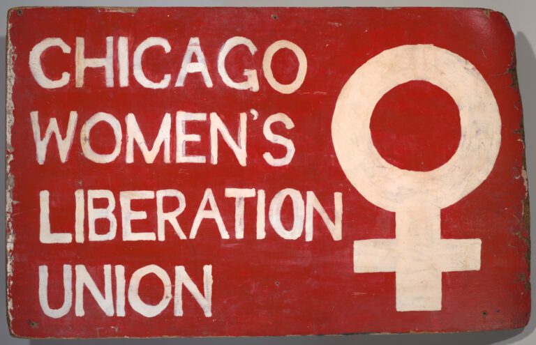 Wooden sign hand-painted red with white letters. Text reads "Chicago Women's Liberation Union" next to a large female symbol. 